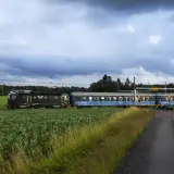 Ett svart lok drar blå sovvagnar på nya nattåg genom ett lantligt landskap med gröna fält och skog.