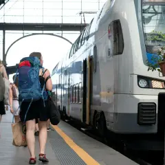 Två unga kvinnor med stora ryggsäckar går längs en tågperrong, redo att tågluffa i Sverige.