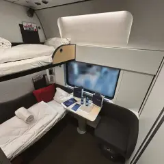 Sovkabin i en Nightjet-tåg med två våningssängar, bord och sittplats. Perfekt för en bekväm resa.