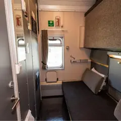 Enkel och ren sovvagn tåg-hytt med en bädd, fönster och förvaring.