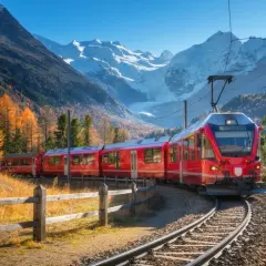 Rött tåg på Bernina Express-linjen, perfekt för Interrail, slingrar sig genom en höstfärgad dal med snöklädda berg i bakgrunden.