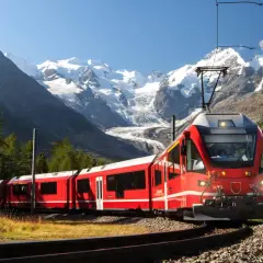Ett rött tåg slingrar sig genom ett berglandskap med snöklädda toppar. Snart är det dags för nattåg till Italien.