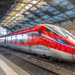 Ett rött snabbtåg i Frankrike, med namnet "Frecciarossa 1000", står på en station under ett glastak.