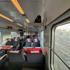 Vy-tåget mot Luleå från Stockholm. Tomma säten med röda bord och fönster med utsikt över snöig skog.