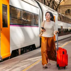 Kvinna med röd resväska och mobiltelefon på tågstationen, redo för sitt tågluffa Europa karta-äventyr.