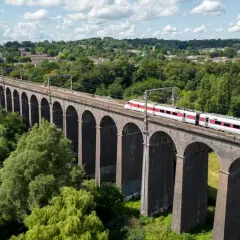 Ett modernt tåg susar fram över en gammal tegelbro, en perfekt bild för att tågluffa i England.