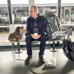 Man och hund väntar på tåget för att tågluffa Skottland. Stor ryggsäck och tidning redo för äventyret.
