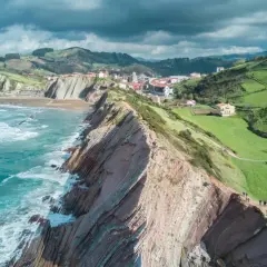 Vacker kustlinje med dramatiska klippor och gröna kullar i **Galicien, Spanien**. Havet sköljer mot stranden.