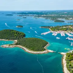En vacker kustlinje i Kroatien med en stor marina full av båtar. En grönskande ö sticker ut i det turkosa vattnet.