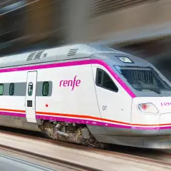 Ett modernt Renfe-tåg i Spanien susar fram längs spåren, med sina distinkta lila och vita färger.