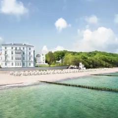 Vacker strand med vita strandstolar och hotell vid den tyska rivieran. Gröna träd och en blå himmel med moln.