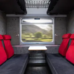 Tomma säten med röda dynor i ett tåg. Utsikten genom fönstret visar ett suddigt landskap, perfekt för en resa med tåg till Storulvån.