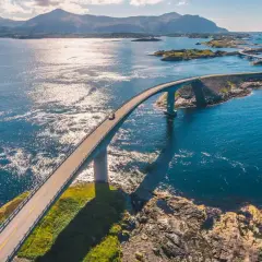 En bil kör på en bro över det glittrande havet i Norge. En dröm för alla som älskar att bila i Norge.
