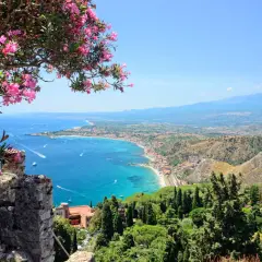 Vacker utsikt över Sicilien med blommande träd i förgrunden. En perfekt plats för vandring med havet och Etna i bakgrunden.