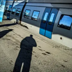 En skugga av en person står vid en tågvagn. En blå skylt med tåg linjer Stockholm syns bredvid.