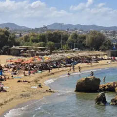 En livlig strand i Grekland med solbadare, parasoller och klippor. En perfekt hotellskatt för en solig semester.