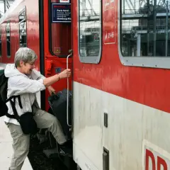 Äldre kvinna med ryggsäck och resväska kliver på ett rött tåg. Kanske början på en resa med interrailkort i Sverige.