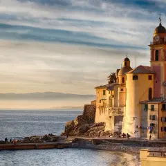 Solnedgång över Camogli, Italien. Kyrkan med sitt klocktorn lyser i kvällssolen vid havet.