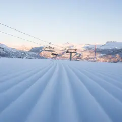 Perfekt pistad backe med sittliftar som tar skidåkare upp mot Hemsedal. Solen lyser på de snöklädda bergen.