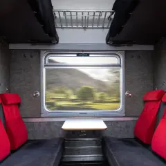 Tomt kupe tåg med röda säten och utsikt över ett grönt landskap i rörelse.