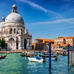 En gondol färdas på Venedigs kanaler framför den ståtliga kyrkan Santa Maria della Salute. En perfekt dag för en resa med tåg till Venedig.
