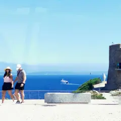 Ett par promenerar vid havet nära ett gammalt torn i Cagliari, Italien.
