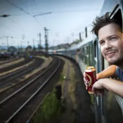 En man lutar sig ut genom tågfönstret med en burk i handen, redo för ett äventyr att tågluffa östeuropa.
