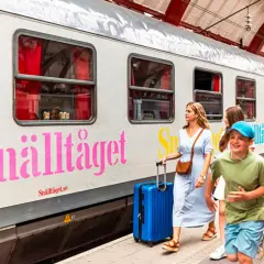 Familj på väg mot Stockholm med Snälltåget. Glada barn och vuxna med resväskor vid tåget.