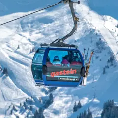 En blå gondol med skidåkare på väg uppför ett snöigt berg. Snart dags för tåg till St. Anton!