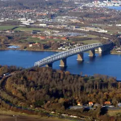 Lilla Bältbron sträcker sig över det blå vattnet, omgiven av höstfärgad skog och en stad i bakgrunden.
