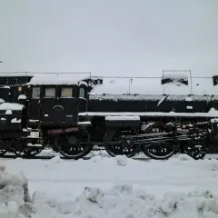 Ett snötäckt ånglok, dekorerat med ljusslingor, står parkerat. Kanske en del av ett biltåg i Tyskland som väntar på våren.