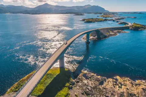 En bil kör på en bro över det glittrande havet i Norge. En dröm för alla som älskar att bila i Norge.