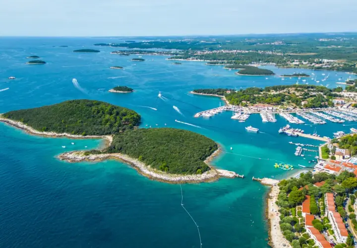 En vacker kustlinje i Kroatien med en stor marina full av båtar. En grönskande ö sticker ut i det turkosa vattnet.