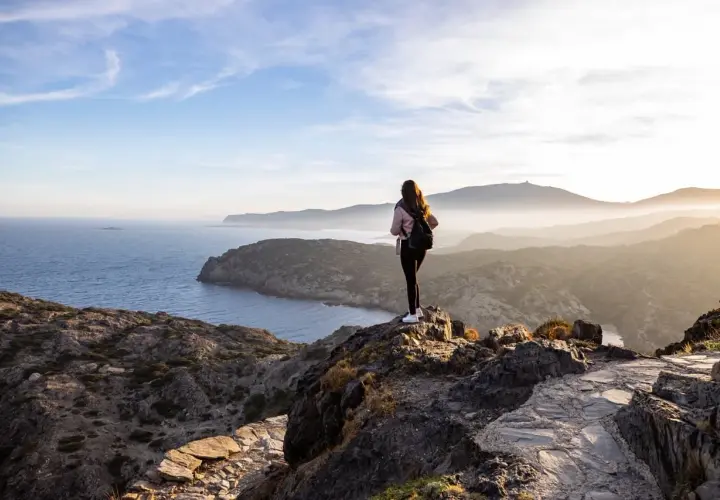 Ensam vandrare njuter av den dramatiska kustlinjen vid Costa Brava. Solen går ner över bergen och havet.