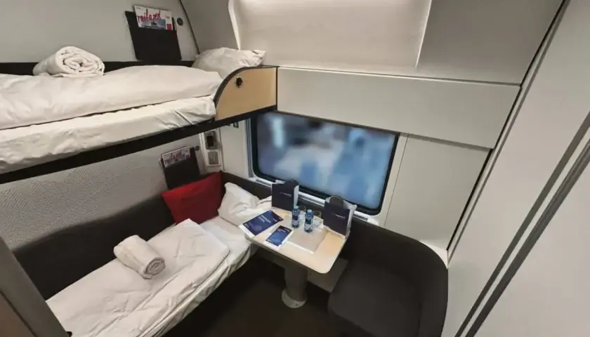 Sovkabin i en Nightjet-tåg med två våningssängar, bord och sittplats. Perfekt för en bekväm resa.