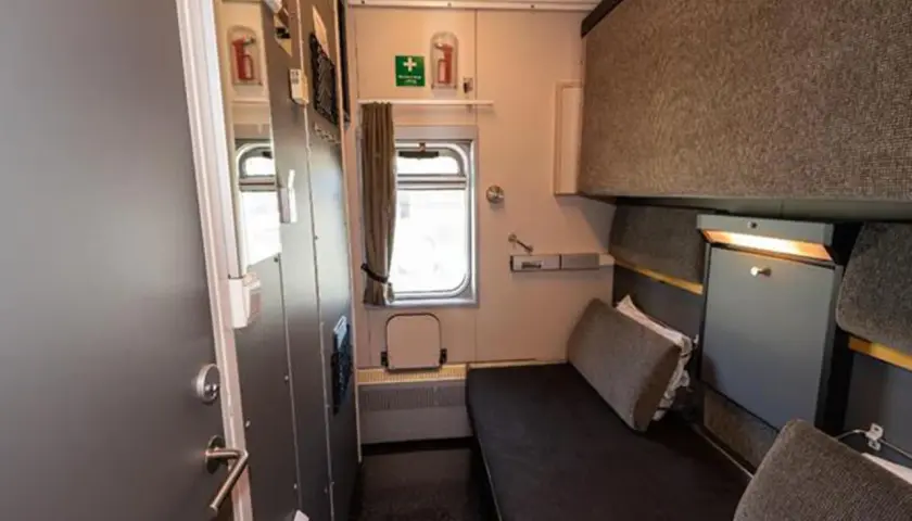 Enkel och ren sovvagn tåg-hytt med en bädd, fönster och förvaring.