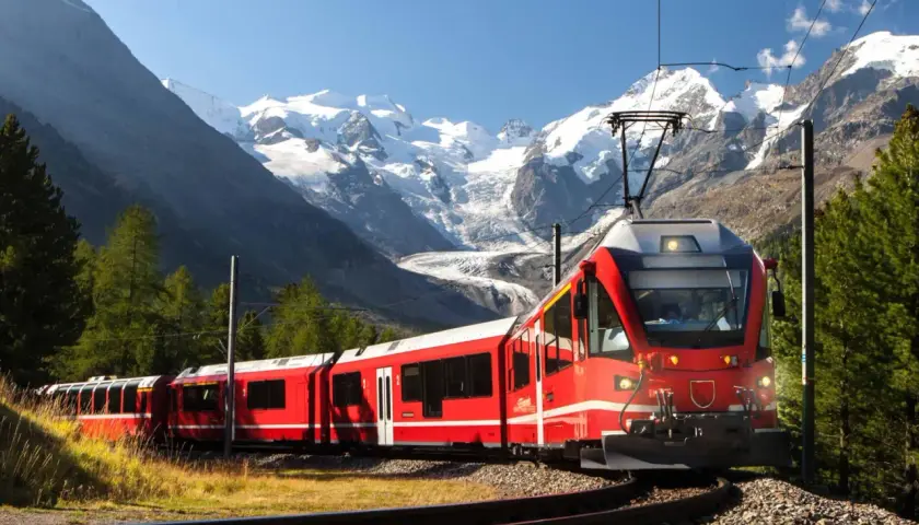 Ett rött tåg slingrar sig genom ett berglandskap med snöklädda toppar. Snart är det dags för nattåg till Italien.