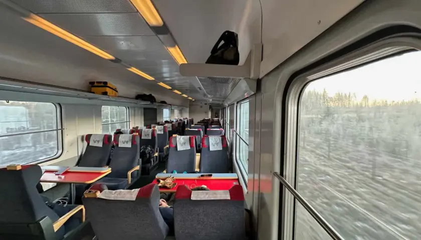 Vy-tåget mot Luleå från Stockholm. Tomma säten med röda bord och fönster med utsikt över snöig skog.