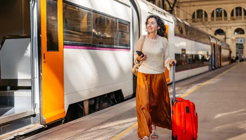 Kvinna med röd resväska och mobiltelefon på tågstationen, redo för sitt tågluffa Europa karta-äventyr.