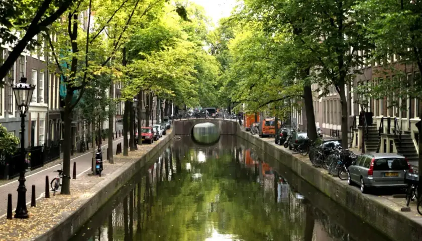 En vacker kanal i Amsterdam, med träd som kantar vattnet. Tänk dig att ta ett tåg från Stockholm till Amsterdam och uppleva denna vy.