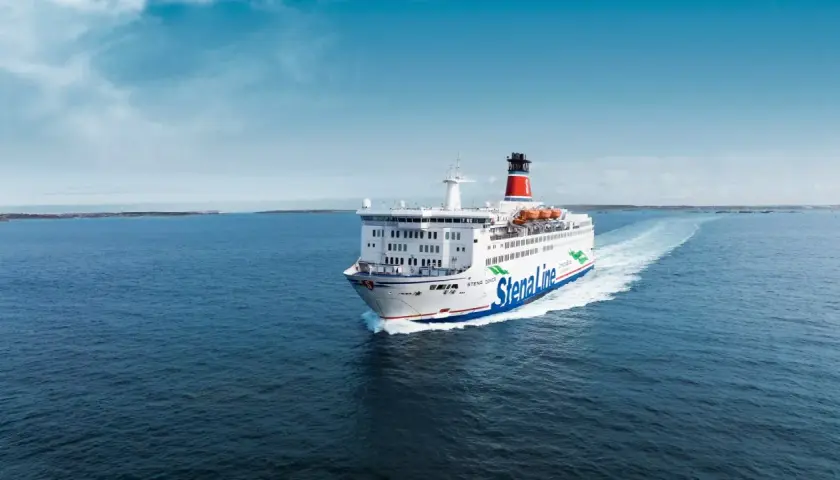 Stena Line-färja på väg till Danmark, med en stor vit skrov och blå linjer, lämnar ett vitt spår i det blå havet under en klarblå himmel.