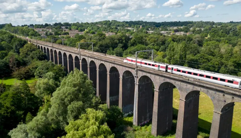 Ett modernt tåg susar fram över en gammal tegelbro, en perfekt bild för att tågluffa i England.