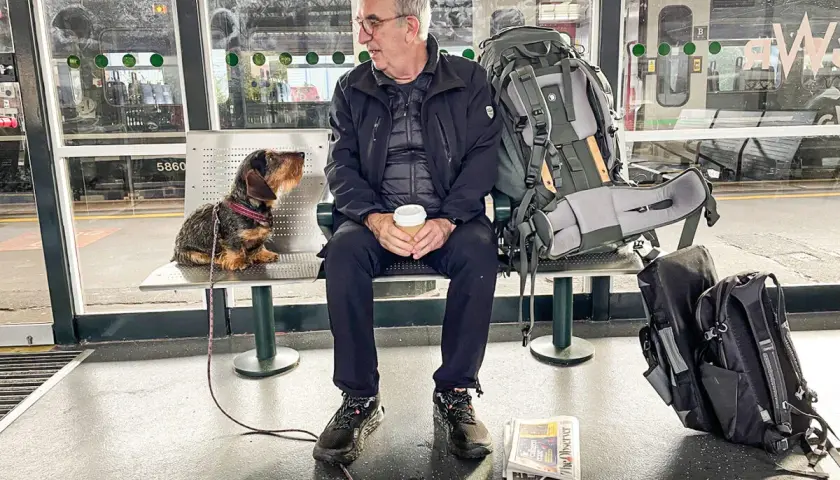 Man och hund väntar på tåget för att tågluffa Skottland. Stor ryggsäck och tidning redo för äventyret.
