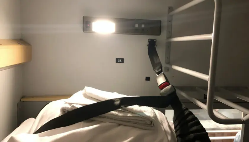 En bädd i en couchette train med vita lakan, handdukar och ett säkerhetsbälte.
