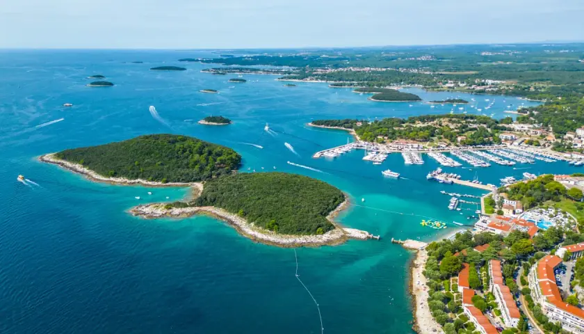 En vacker kustlinje i Kroatien med en stor marina full av båtar. En grönskande ö sticker ut i det turkosa vattnet.