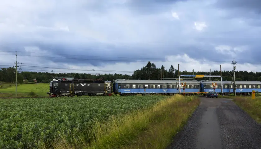 Ett svart lok drar blå sovvagnar på nya nattåg genom ett lantligt landskap med gröna fält och skog.