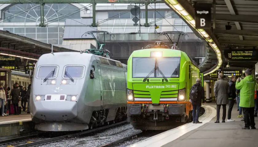 Två tåg, ett silverfärgat och ett grönt FlixTrain, står vid perrongen. En perfekt start för en paketresa tåg Sverige.