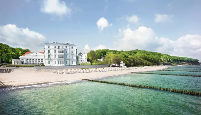 Vacker strand med vita strandstolar och hotell vid den tyska rivieran. Gröna träd och en blå himmel med moln.