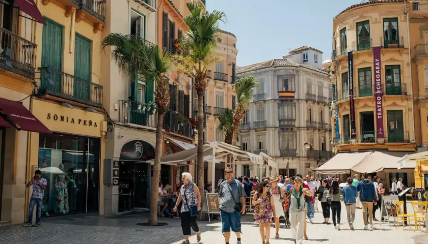 Folk promenerar på en solig gata i Malaga, kanske på väg till tågstationen för en resa till Stockholm.