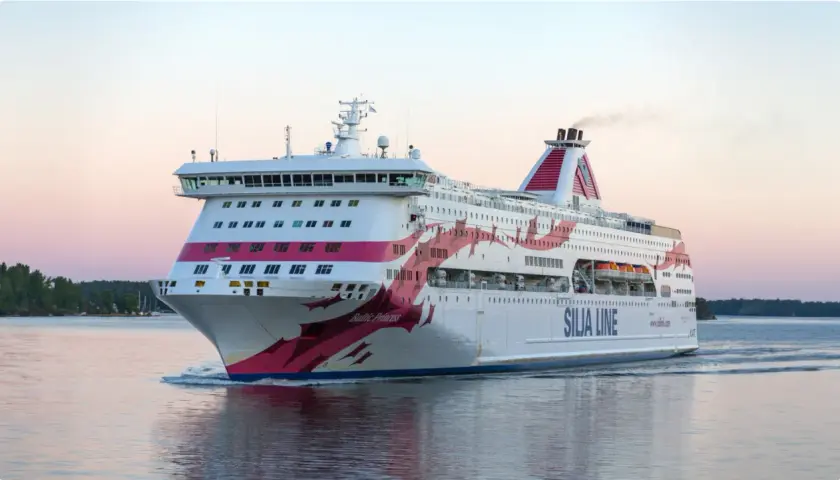 Silja Line-färja på en kryssning Stockholm-Åbo. En stor vit passagerarfärja med rosa dekorationer glider fram på vattnet i solnedgången.